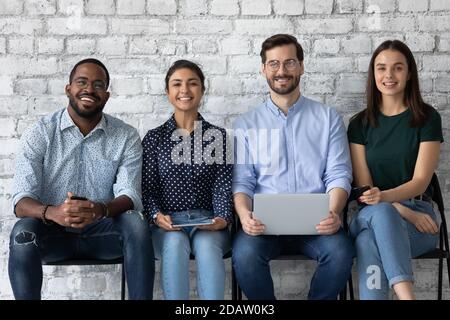 Des amis multiethniques heureux et confiants, assis dans la rangée, tenant des téléphones, des ordinateurs Banque D'Images