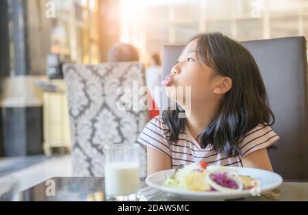 Enfant fille asiatique avec expression de dégoût à l'égard des légumes dans un restaurant, refusant food concept Banque D'Images