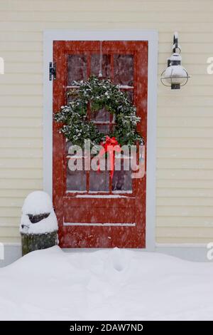 Une couronne de Noël est suspendue sur une porte rouge dans une maison de Phillipston, Massachusetts Banque D'Images