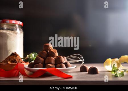 Pile de truffes au chocolat fraîchement préparées pour un événement spécial sur une table en bois avec des ingrédients et un fond sombre vue de face. Composition horizontale. Banque D'Images