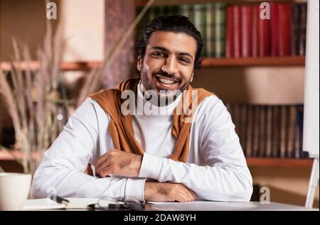 Portrait du jeune homme enseignant indien souriant assis sur le lieu de travail Banque D'Images