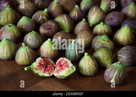 Une figue fraîchement cueillie “Ficus carica” déchirée en deux pour révéler les graines et la chair rouge succulente. Sur fond de figues disposées sur une table en bois. Banque D'Images