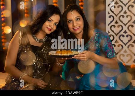 Portrait de deux indiennes partageant des bonbons à l'occasion de la fête de Diwali. Fêtes à la maison. Banque D'Images