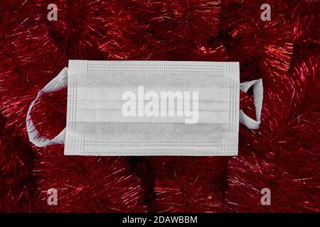 Flat lay décoration de noël festive et masque de protection médicale du visage sur fond rouge scintillant Banque D'Images