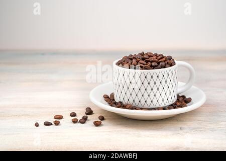 Fond de café, les grains de café sont versés dans une tasse sur fond clair. Banque D'Images