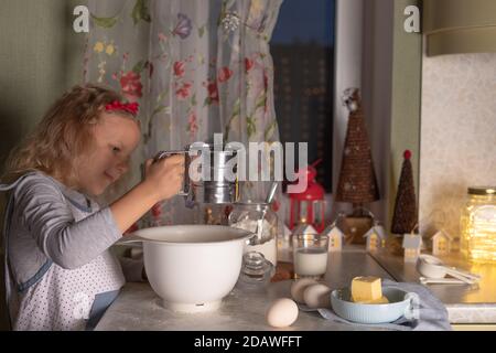 Petite fille heureuse tamisant la farine et préparant la pâte dans le Cuisine le soir de Noël Banque D'Images