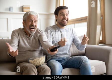 Père mûr et joyeux, son fils regardant la télévision, s'amusant ensemble Banque D'Images