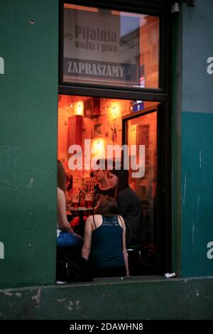 Clients de Lady dans une table lumineuse à fenêtre photographiée de l'extérieur à Wodki i Piwa, un café-restaurant renommé de Cracovie à Kazimiers. Banque D'Images