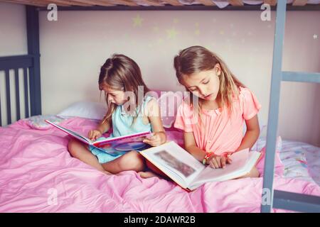 Joyeuses sœurs caucasiennes filles lisant des livres dans la chambre. Les enfants frères et sœurs à la maison passent du temps ensemble. Apprentissage du développement de l'éducation des enfants. Banque D'Images