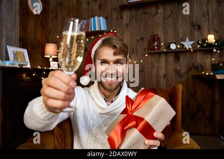 Joyeux homme portant un chapeau de père noël tenant un cadeau de Noël regardant l'appareil photo. Banque D'Images