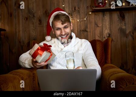 Jeune homme heureux célébrant la fête virtuelle en ligne du nouvel an à l'aide d'un ordinateur portable. Banque D'Images