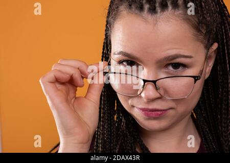 Une jeune fille adulte règle doucement ses lunettes. Étudiant de dernière année. Un regard passionné sur l'objectif. Banque D'Images