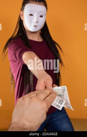 La main masculine prend l'argent d'un étranger qui a un masque sur tout son visage pour que personne ne le reconnaisse. A promis de l'argent dans un prêt anonyme. Banque D'Images