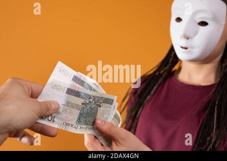 La main masculine prend l'argent d'un étranger qui a un masque sur tout son visage pour que personne ne le reconnaisse. A promis de l'argent dans un prêt anonyme. Banque D'Images