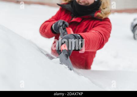 L'homme en rouge avec capuche fourrure manteau d'hiver voiture nettoyage après la tempête de neige Banque D'Images