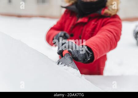 L'homme en rouge avec capuche fourrure manteau d'hiver voiture nettoyage après la tempête de neige Banque D'Images