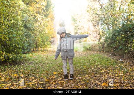 Jolie petite fille volant avec des bras ouverts comme un avion En automne, parc ensoleillé ou forêt - Portrait de petite fille debout dans les bois pendant le feuillage Banque D'Images