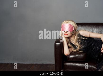 Une femme avec un masque de sommeil rose se trouve sur le canapé avec une bouteille de bière dans la main Banque D'Images