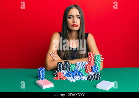 Jeune femme hispanique assis sur la table jouant au poker sceptique et nerveux, désapprouvant l'expression sur le visage avec les bras croisés. Personne négative. Banque D'Images