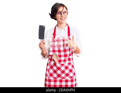 Belle jeune femme aux cheveux courts portant un tablier de boulanger professionnel tenir le couteau sourire heureux de pointer avec la main et le doigt Banque D'Images