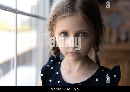 Portrait de petite fille d'âge scolaire sérieuse debout par fenêtre Banque D'Images