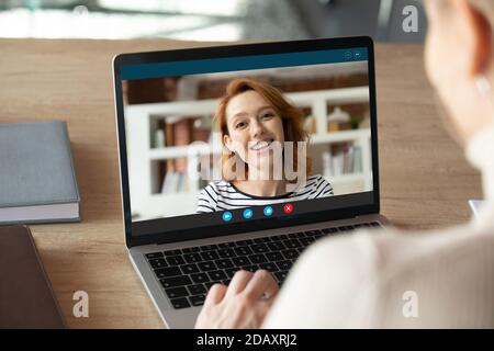Une femme souriante aux cheveux rouges qui tient un appel vidéo avec un collègue. Banque D'Images