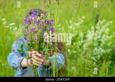 Bouquet de cloches de prairie et autres fleurs sauvages dans les mains d'une jeune fille marchant dans le champ. Banque D'Images