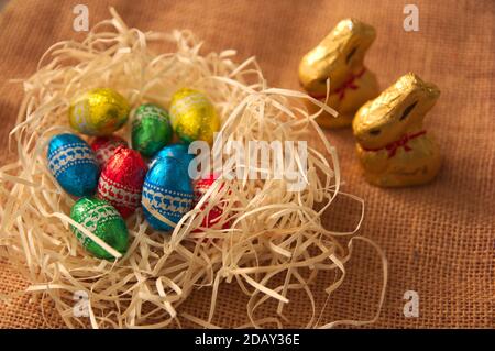 Gros plan de quelques oeufs de chocolat qui sont dans une pile de paille à côté de quelques lapins dorés. Arrière-plan pour pâques Banque D'Images