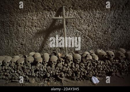 Croix placée sur des crânes et des os humains empilés au cimetière Fontanelle (Cimitero delle Fontanelle) à Naples, Campanie, Italie. L'ancienne maison de charnel (ossuary) située dans une grotte dans le district de Materdei était l'endroit où le culte spontané de la dévotion aux restes de morts sans nom s'est développé à Naples. Les défenseurs du culte ont payé des visites aux crânes sans nom dans l'ossuaire pour les adopter et même donner les noms des crânes. Les crânes adoptés ont été placés à l'intérieur de la boîte décorée et sont devenus l'objet de prières régulières et d'offrande votive. Banque D'Images