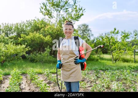 Femme paysanne avec pulvérisateur à main sac à dos protégeant les jeunes plants de pommes de terre Banque D'Images