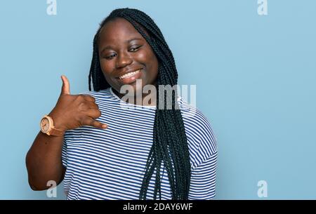 Jeune femme noire avec des tresses portant des vêtements décontractés souriant faisant un geste de téléphone avec la main et les doigts comme parler au téléphone. Communication co Banque D'Images