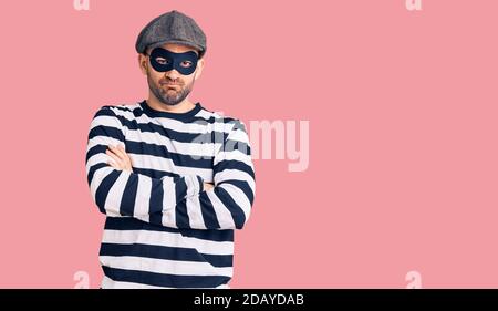 Jeune homme beau portant un masque cambrioleur sceptique et nerveux, désapprouvant l'expression sur le visage avec les bras croisés. Personne négative. Banque D'Images