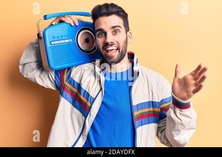 Jeune homme beau avec barbe, écoutant de la musique avec vintage boombox célébrant la réussite avec un sourire heureux et l'expression du gagnant avec main levée Banque D'Images