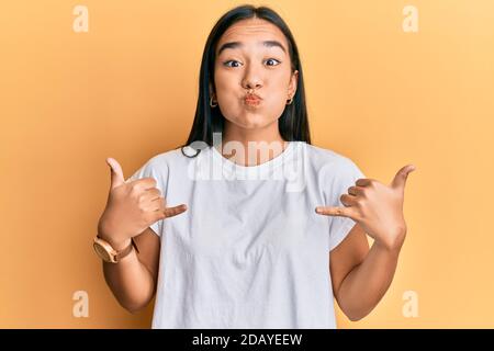 Jeune femme asiatique faisant shaka signe avec les mains puffant les joues avec le visage drôle. Bouche gonflée avec l'air, attrapant l'air. Banque D'Images