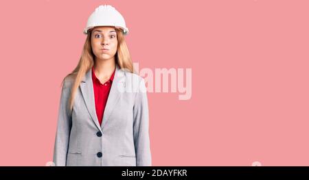 Belle jeune femme portant un architecte hardhat puffing joues avec visage drôle. Bouche gonflée avec de l'air, expression folle. Banque D'Images