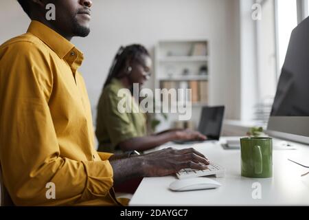 Vue rognée sur le côté d'un jeune homme afro-américain utilisant un PC dans un bureau moderne et en tapant tout en regardant l'écran d'ordinateur, l'espace de copie Banque D'Images