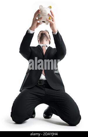 un homme d'affaires kneeing tenant une tirelire au-dessus de sa tête devant lui d'arrière-plan blanc Banque D'Images