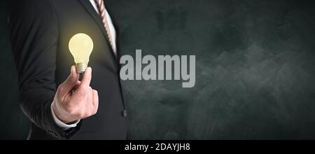 homme d'affaires tenant une ampoule allumée devant un tableau noir Banque D'Images
