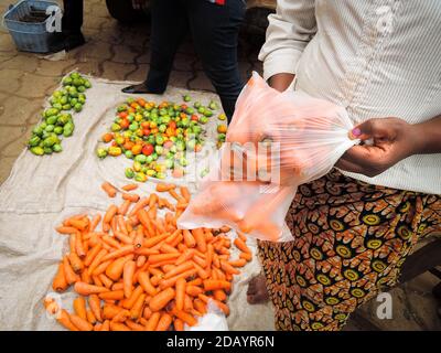 Un vendeur du marché utilise des sacs en plastique pour emballer les carottes achetées par sa cliente au Cameroun. Banque D'Images