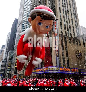 Le ballon Elf on the Shelf flotte dans les airs pendant le défilé de Thanksgiving de Macy le long de l'avenue des Amériques avec radio Music Hall en arrière-plan. Banque D'Images