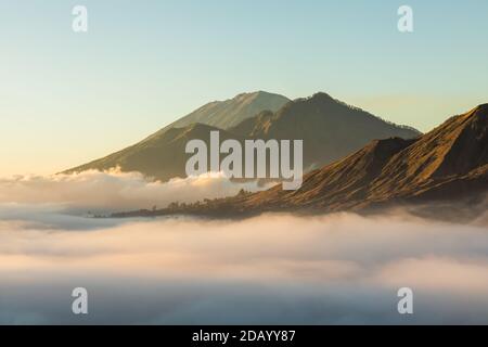 Vue au lever du soleil sur le mont Batur, Abang et le volcan Agung à Bali depuis le village de Pinggan. Beau lever de soleil et nuages bas. Paysage minimaliste superposé. Banque D'Images