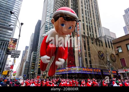 Le ballon Elf on the Shelf flotte dans les airs pendant le défilé de Thanksgiving de Macy le long de l'avenue des Amériques avec radio Music Hall en arrière-plan. Banque D'Images