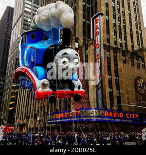 Thomas le Tank Engine flotte dans les airs pendant la parade de Thanksgiving de Macy le long de l'avenue des Amériques avec la radio Music Hall en arrière-plan. Banque D'Images