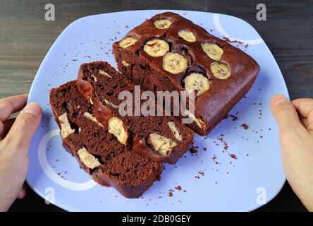 Main de l'homme tenant une assiette de chocolat noir frais Gâteau à la banane placé sur la table Banque D'Images