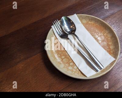 Cuillère et fourchette en acier inoxydable sur une serviette blanche propre sur une plaque en céramique circulaire de style vintage sur une table en bois avec espace de copie. Banque D'Images