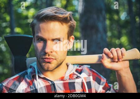 Bûcheron avec hache dans ses mains. Beau jeune homme avec hache près de la forêt. Le bois de chauffage comme source d'énergie renouvelable. Homme faisant des hommes travail. Repos après har Banque D'Images