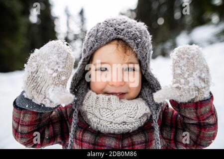 Vue de face portrait d'une petite fille gaie debout dans la nature d'hiver, regardant l'appareil photo. Banque D'Images