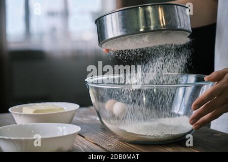 Les mains des femmes tamisent la farine dans un bol en verre Banque D'Images