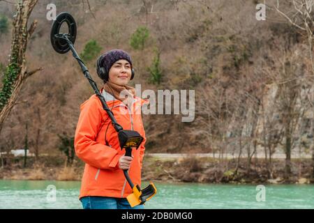Rechercher avec UN détecteur de métal. Une jeune femme posant avec un détecteur de métal sur le fond de la rivière. Gros plan. Banque D'Images