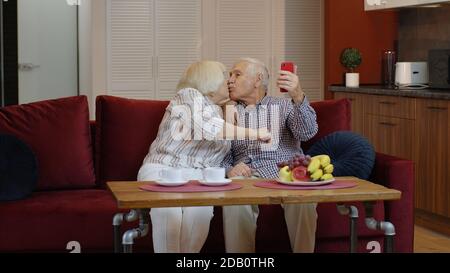 Famille senior s'amusant, faisant des photos de selfie ensemble sur smartphone à la maison. Riing liant mature couple marié plus ancien en utilisant des applications drôles de téléphone mobile ou d'enregistrement vidéo. Faire un baiser